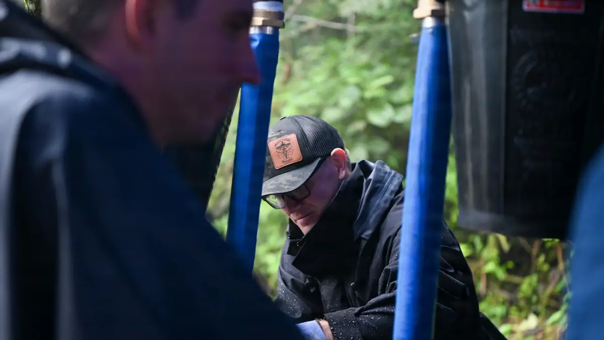 Two workers repairing blue water pipes outdoors among greenery - Leak Detection in Des Plaines